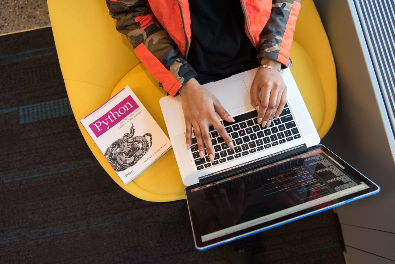 hero-img A developer typing code on a laptop with a Python book beside in an office.